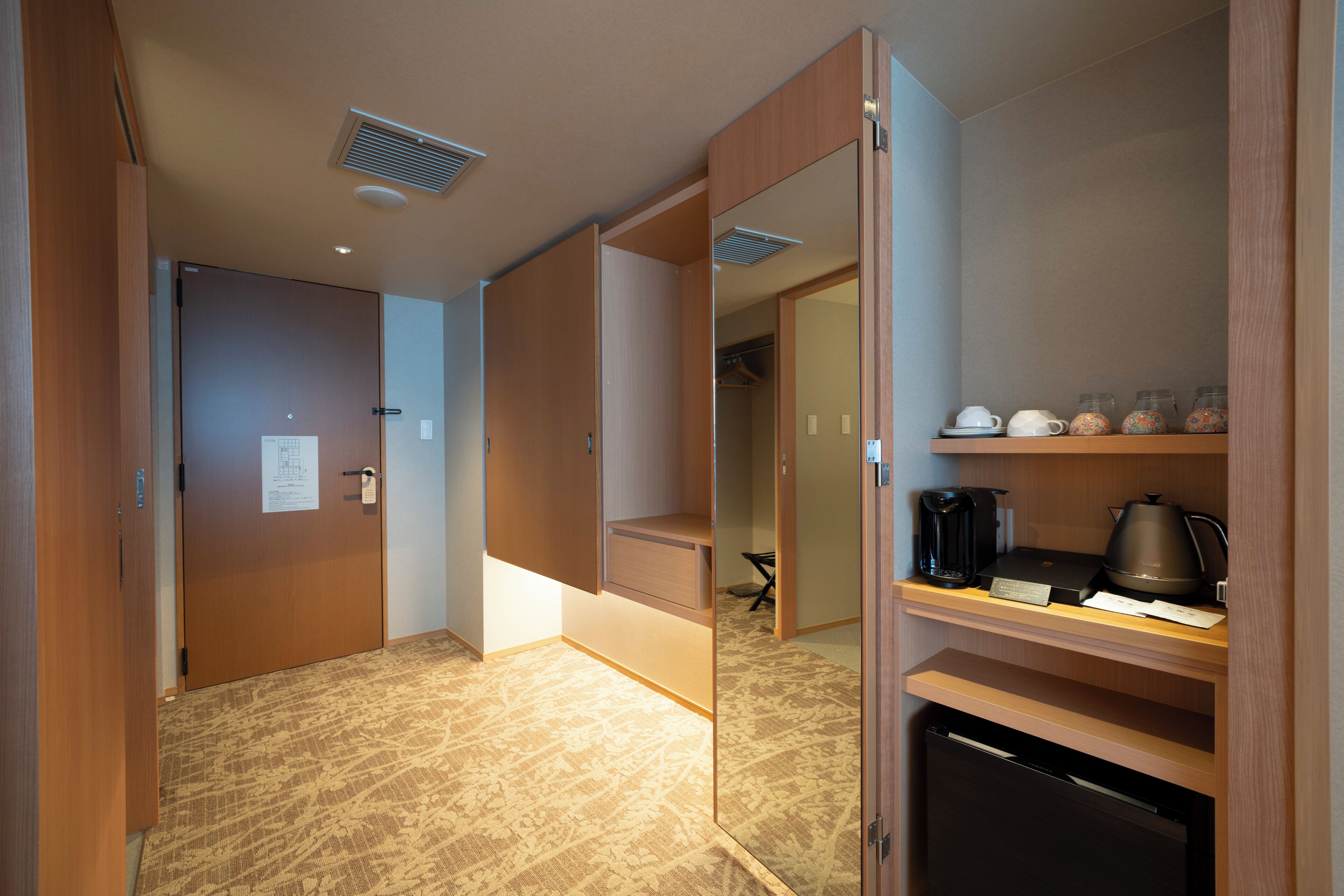 A hotel room with a wardrobe, a small kitchenette, and a mirror.