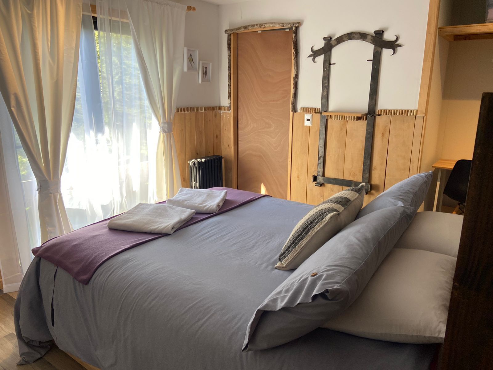 A bedroom with a bed, a radiator, wooden paneling, and a rustic metal headboard.