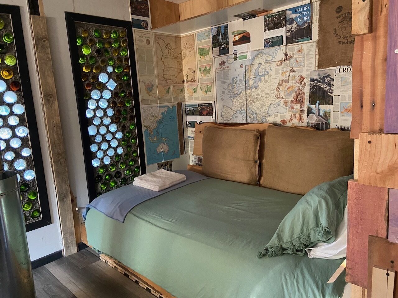 A bed with a green bedspread, pillows, and a map-covered wall.