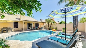 Un patio trasero con piscina, sillas de descanso, una mesa y un parasol.