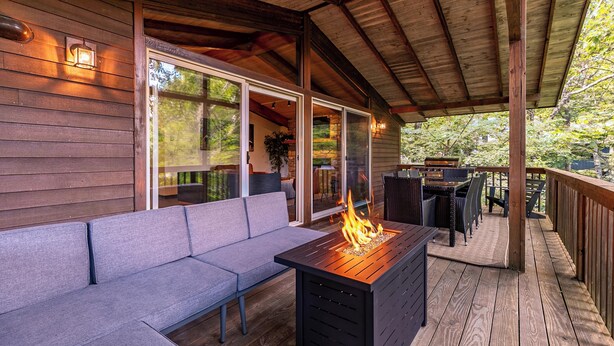 Eine überdachte Terrasse mit einer Holzbank, einem Feuerkorb und Blick auf die umliegende Bepflanzung.
