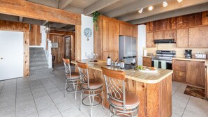 A kitchen with wooden cabinets, a stainless steel refrigerator, a built-in oven, and a bar area with stools. - Rustic Oceanfront Cabin (Dillon Beach)