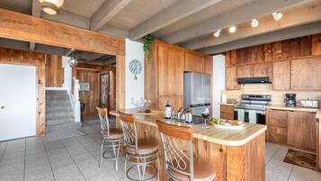 A kitchen with wooden cabinets, a stainless steel refrigerator, a built-in oven, and a bar area with stools.