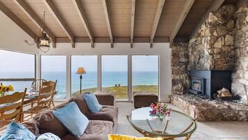 Una sala de estar acogedora con chimenea de piedra, una mesa de centro de vidrio y vistas al océano.