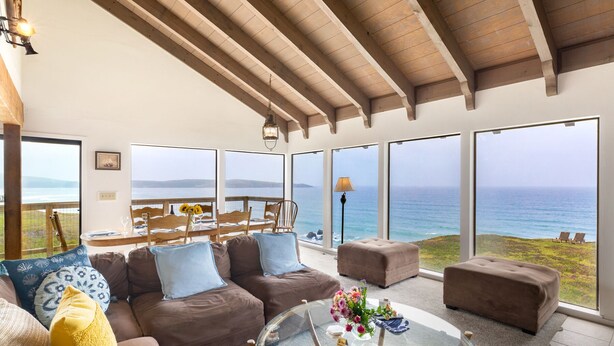 A spacious living room with a large glass table, comfortable seating, and a view of the ocean. - Rustic Oceanfront Cabin (Dillon Beach)