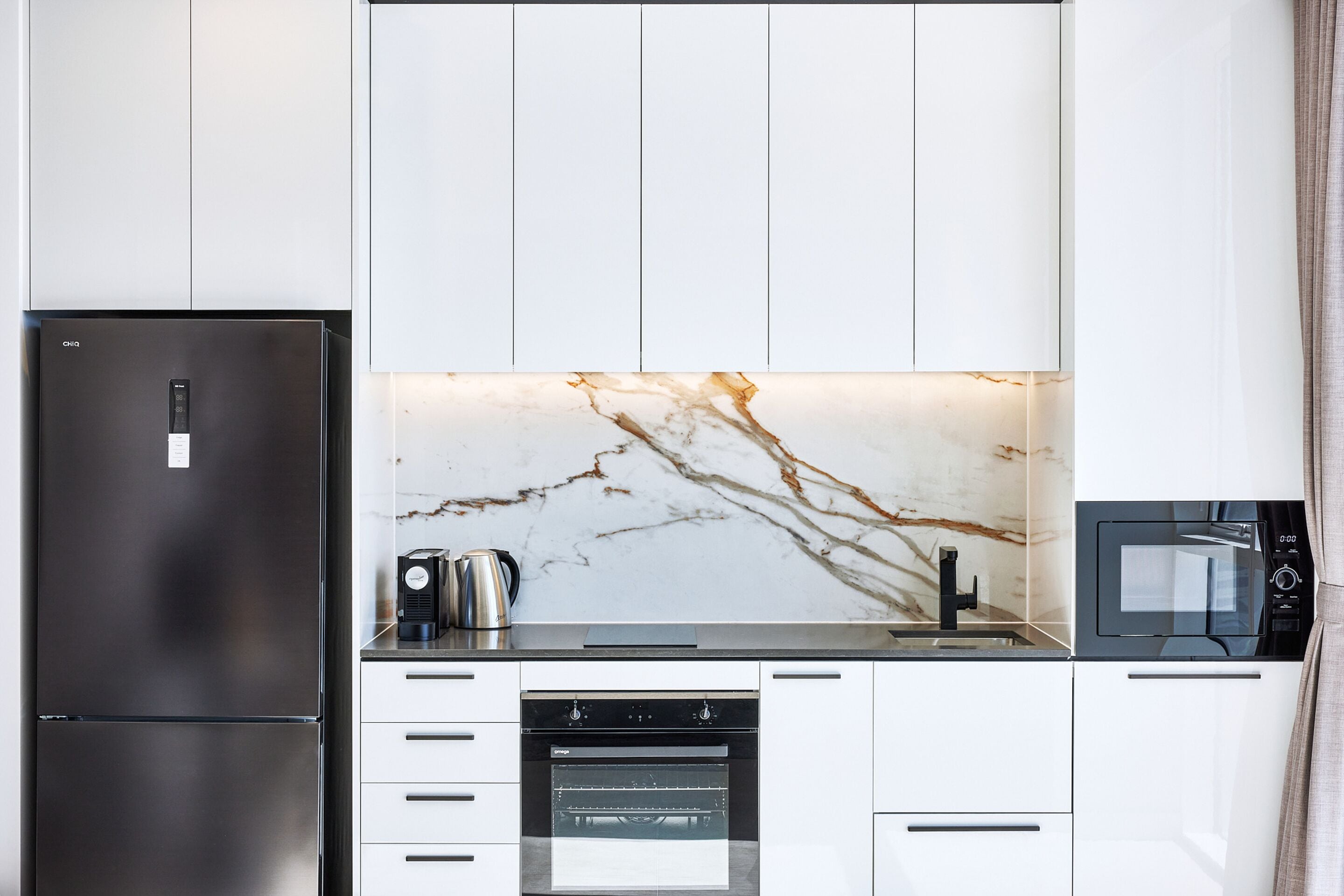 A modern kitchen with a stainless steel refrigerator, a built-in oven, and a microwave.