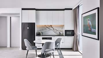A modern kitchen with white cabinets, a black refrigerator, a marble backsplash, and a dining area with grey upholstered chairs.