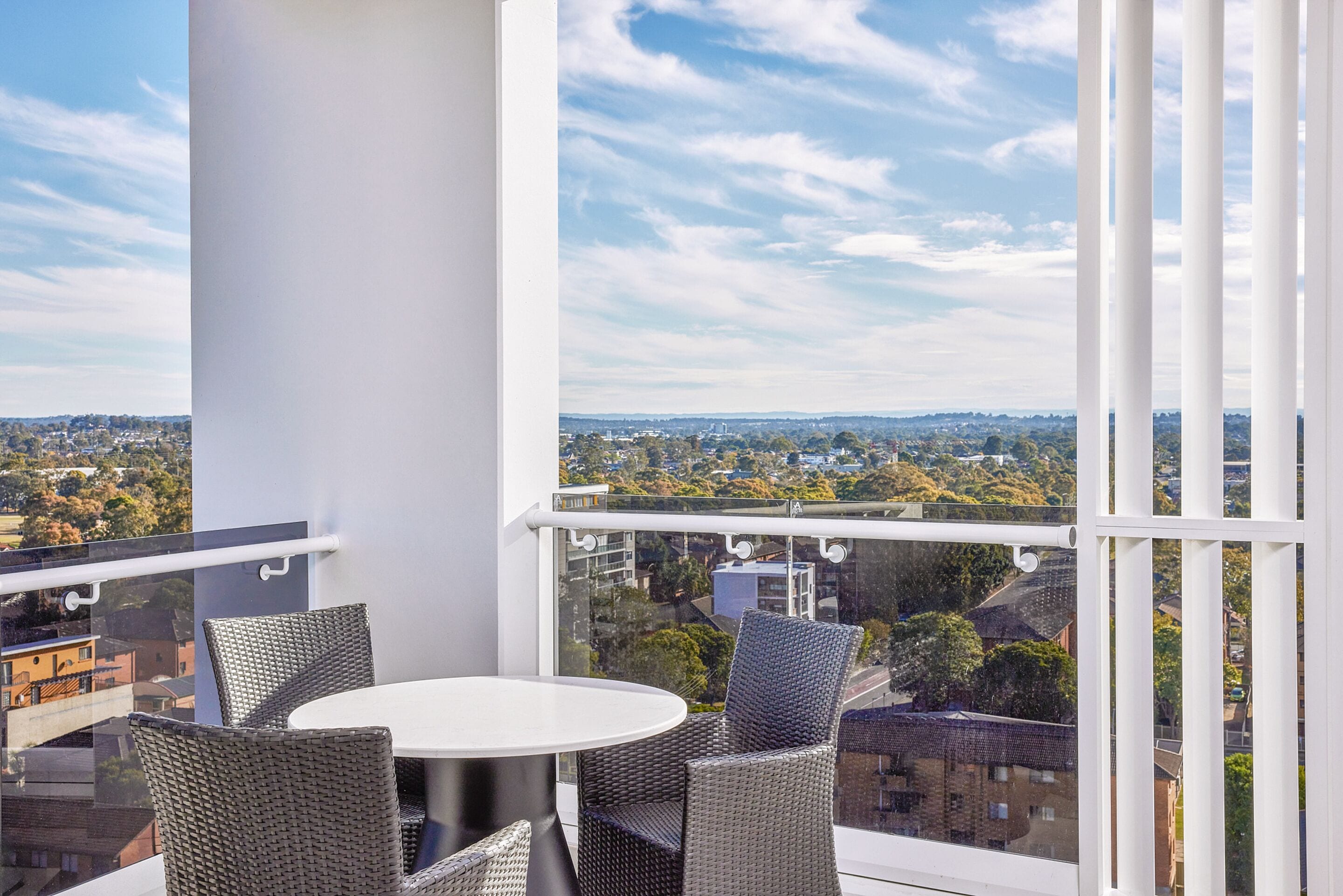 A balcony with wicker chairs and a table, offering a view of a cityscape.