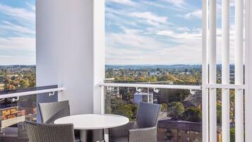 A balcony with wicker chairs and a table, offering a view of a cityscape.