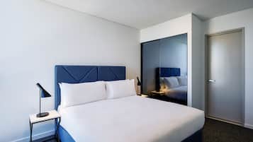 A modern hotel room with a large bed, a nightstand, a lamp, and a wardrobe.