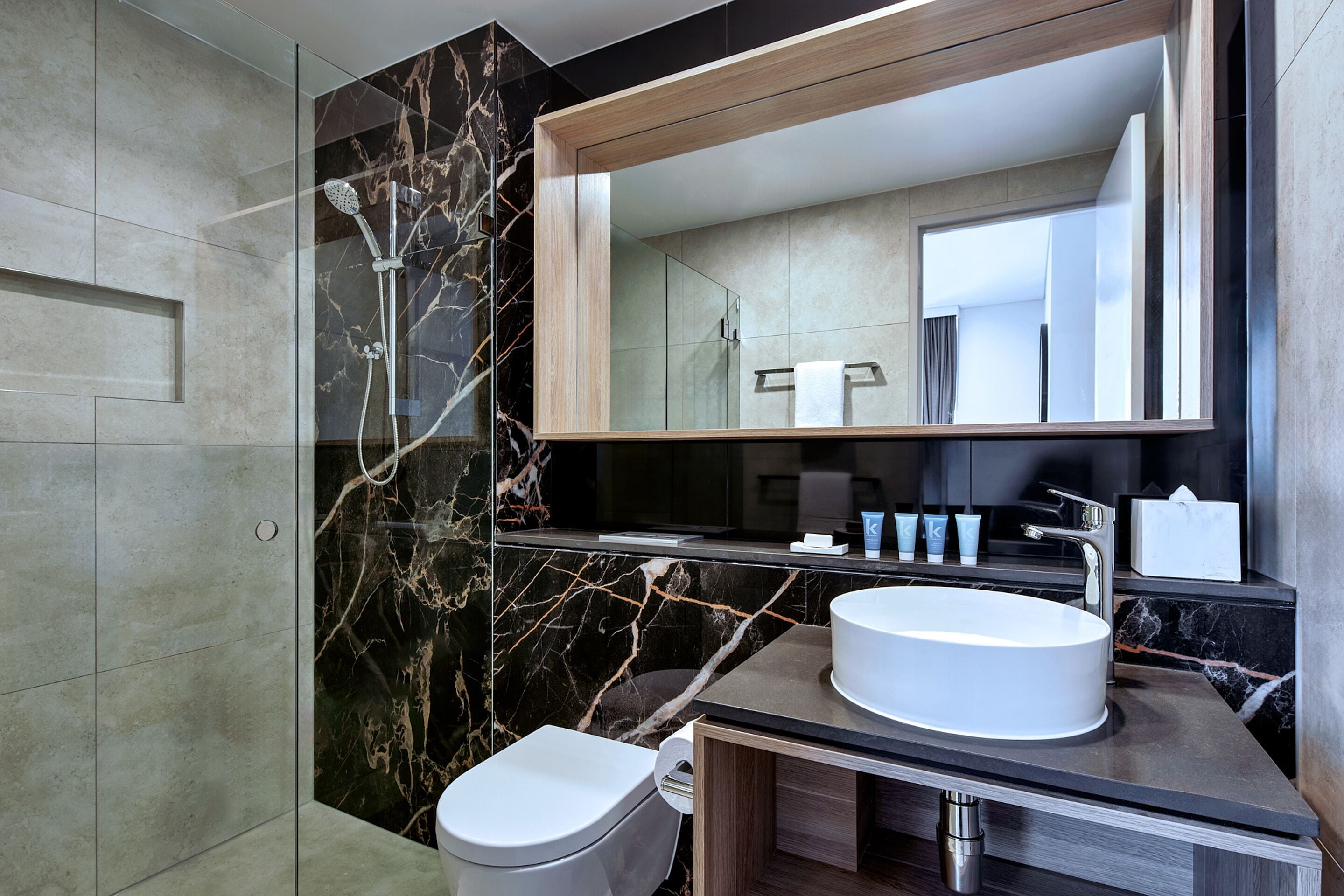 A modern bathroom with a large mirror, two sinks, a toilet, and a shower area.