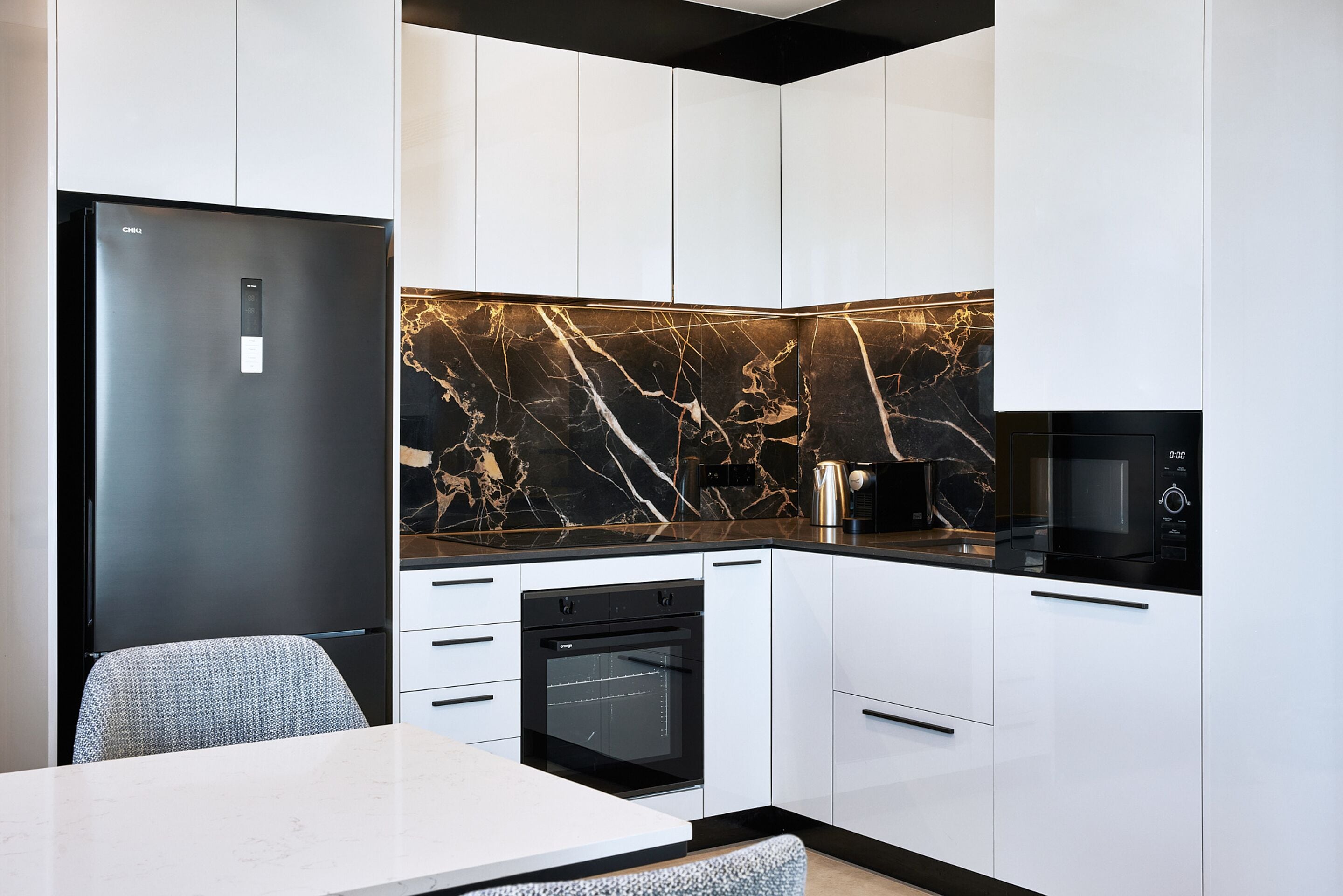 Eine moderne Küche mit weißen Schränken, einem schwarzen Kühlschrank, einem eingebauten Backofen und einer Marmor-Spritzschutzwand.