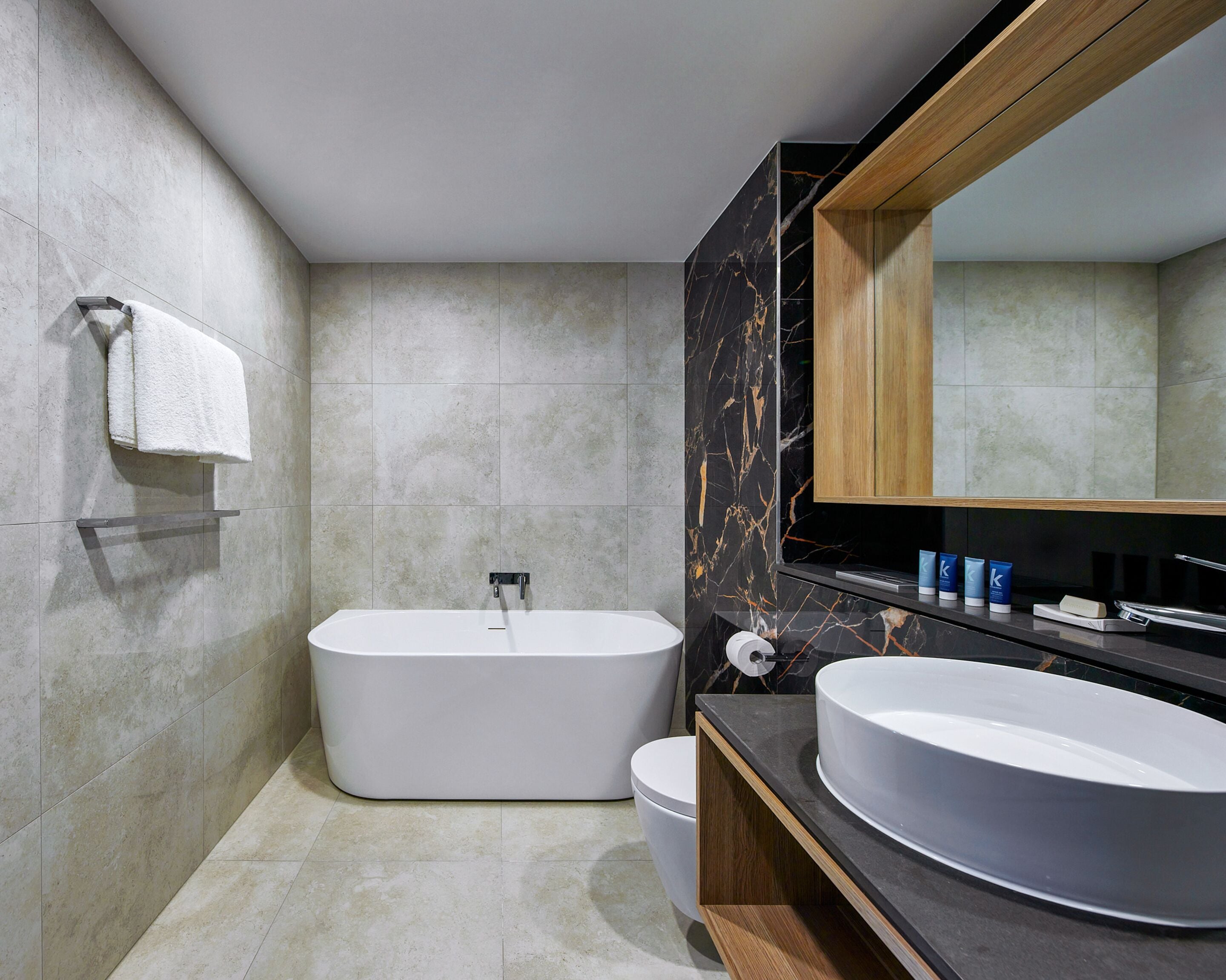 A modern bathroom with a freestanding bathtub, a large vanity with a round sink, and a wooden-framed mirror.