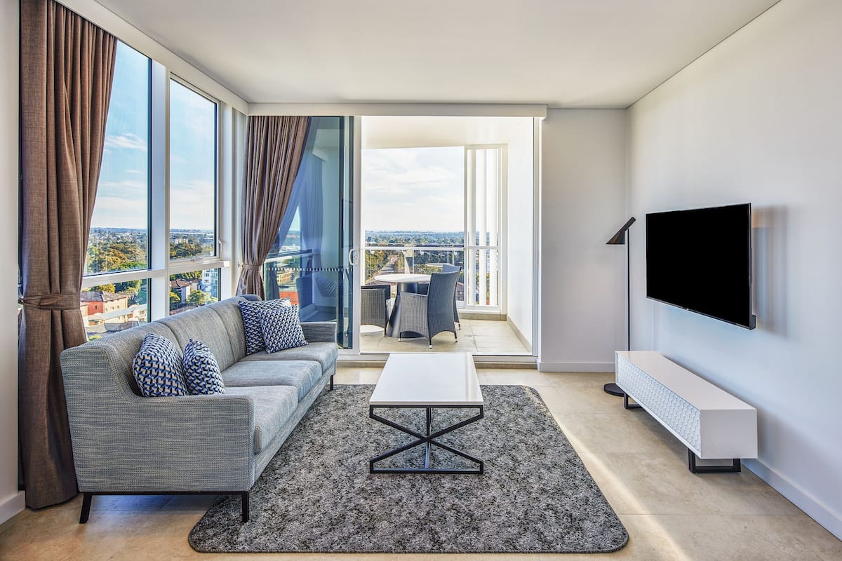A modern living room with a grey sofa, patterned cushions, a white coffee table, and a large TV.