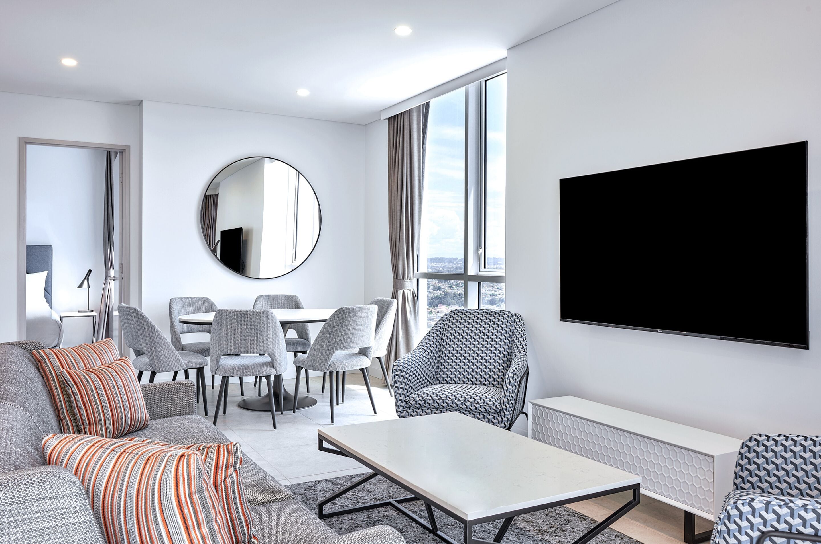Un salon moderne comprenant un canapé, un fauteuil, une table à manger, des chaises et un téléviseur.