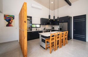 Une cuisine moderne avec des meubles de couleur sombre, un îlot central, des chaises en bois et des luminaires suspendus.