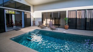 A modern indoor pool area with a clear view of the pool, lounge chairs, and a staircase leading to a deck area.