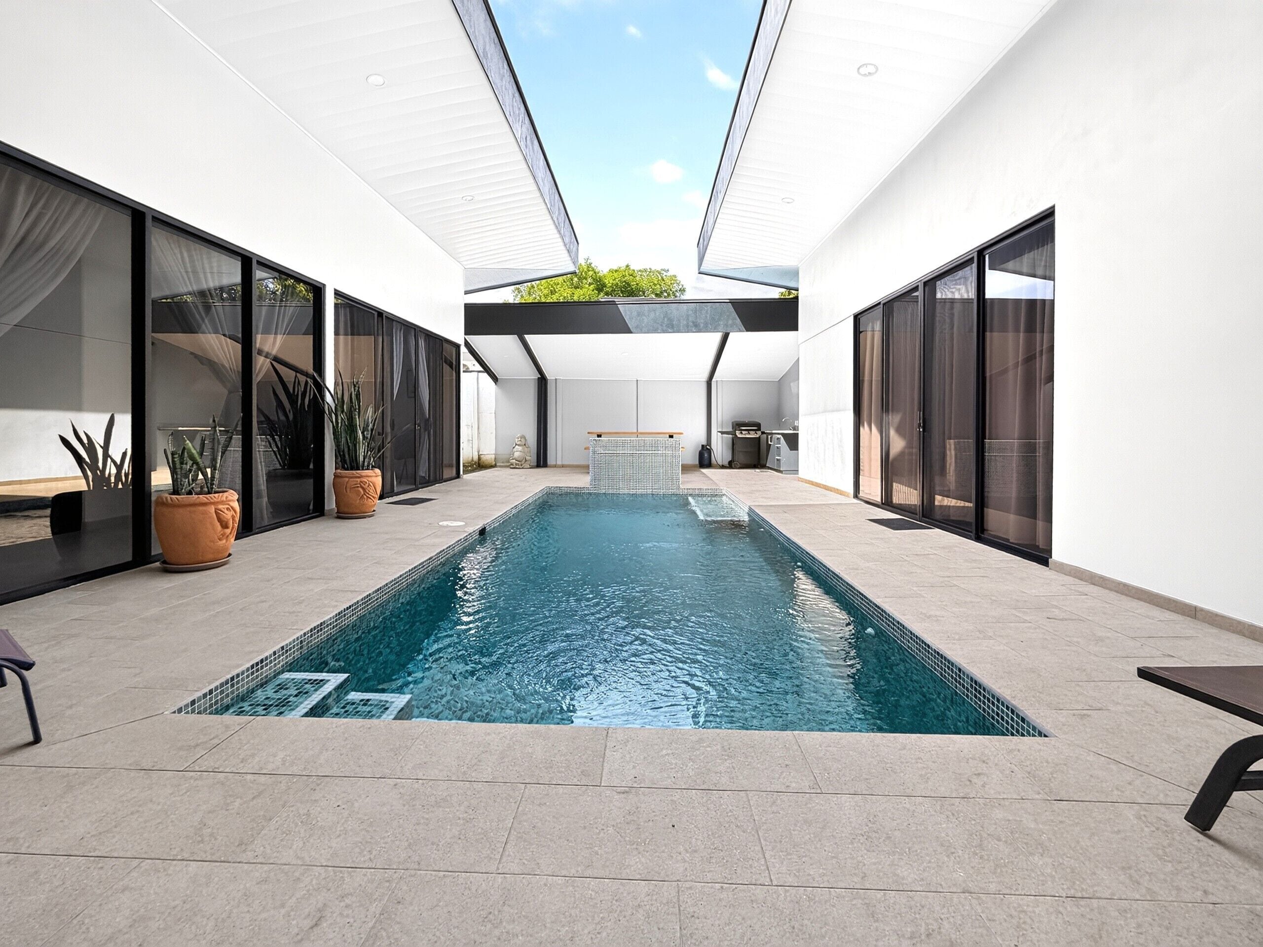 A modern indoor swimming pool with clear blue water, surrounded by glass walls and potted plants.