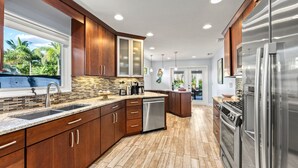 A modern kitchen with wooden cabinets, stainless steel appliances, and a herringbone tile floor. - Mermaids Oasis | Private Pool, Hot Tub, & 5 Minute Walk to St. Armands Circle & Lido Key Beach! (Lido Key)