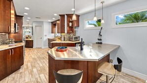 A modern kitchen with wooden cabinets, a central island, pendant lighting, and a view of the outdoors. - Mermaids Oasis | Private Pool, Hot Tub, & 5 Minute Walk to St. Armands Circle & Lido Key Beach! (Lido Key)