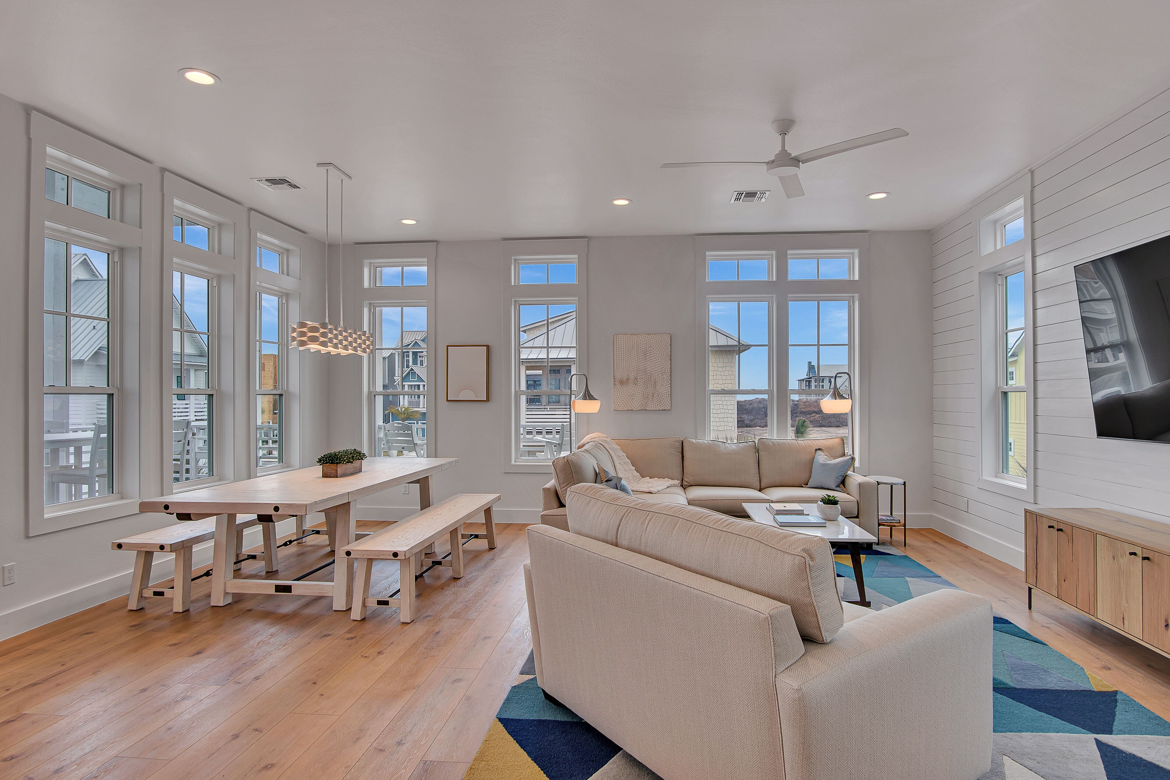 A spacious living room with a large sofa, a dining table with benches, and a TV.