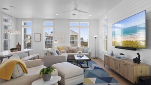 A spacious living room with a large TV, comfortable seating, and a view of the ocean. - Game Room, Resort Pools, Golf Cart Boardwalk to the Beach (Port Aransas)