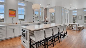 A modern kitchen with white cabinetry, a large island with bar stools, and pendant lighting. - Game Room, Resort Pools, Golf Cart Boardwalk to the Beach (Port Aransas)