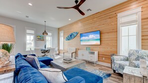 A modern living room with a blue sofa, white coffee table, and a ceiling fan. - Resort Pools, Golf Cart Boardwalk to Beach, Pet Friendly (Port Aransas)