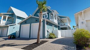 A two-story house with a blue exterior, a white garage door, and a small front yard with a palm tree.