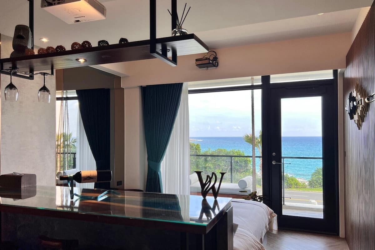 A modern bedroom with a glass-enclosed balcony, a large bed, and a minimalist design.