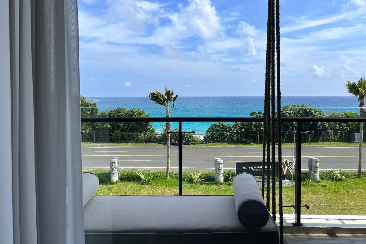 A view from a balcony with a clear ocean and sky, featuring a road with a statue and a sign.