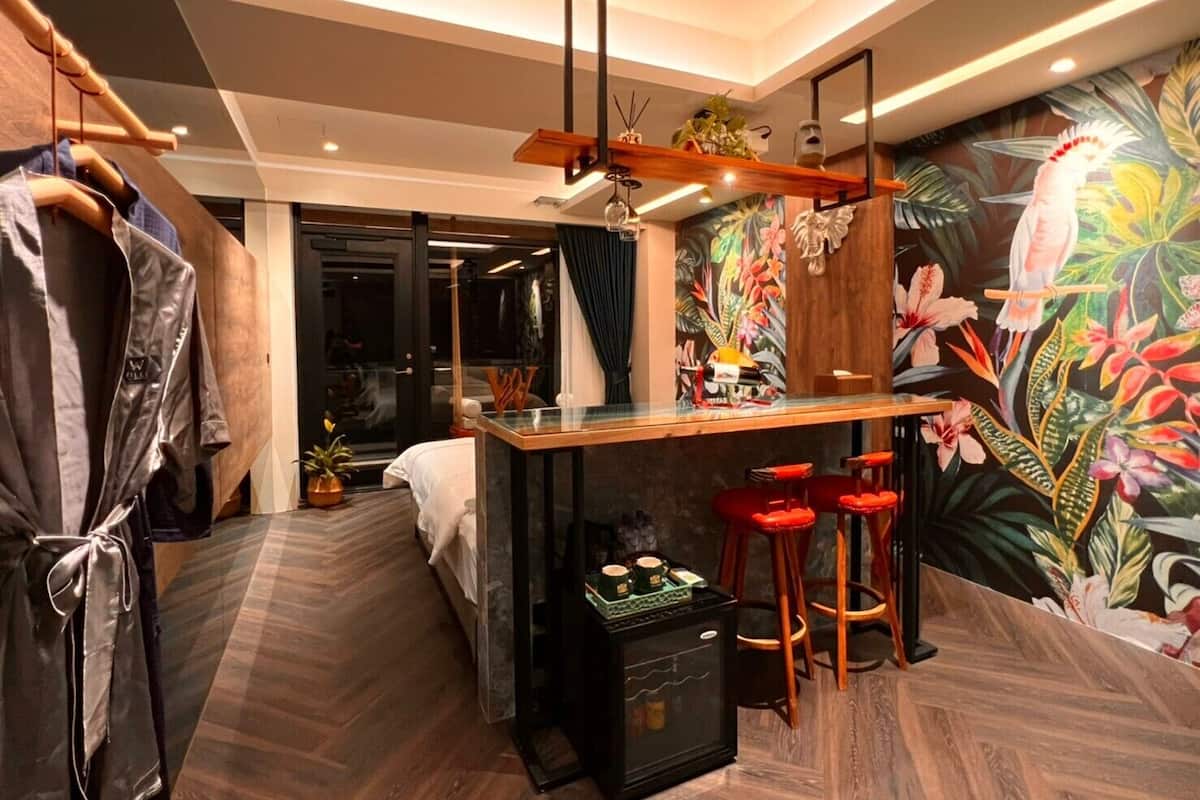 A hotel room with a bar area, a bed, a wardrobe, and a tropical mural.