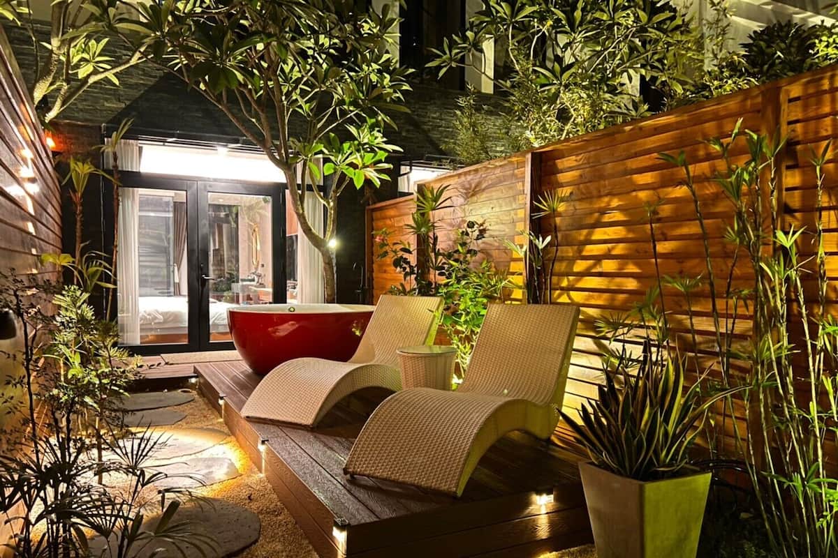 A cozy outdoor seating area with a wooden bench and chairs, surrounded by lush greenery and potted plants.