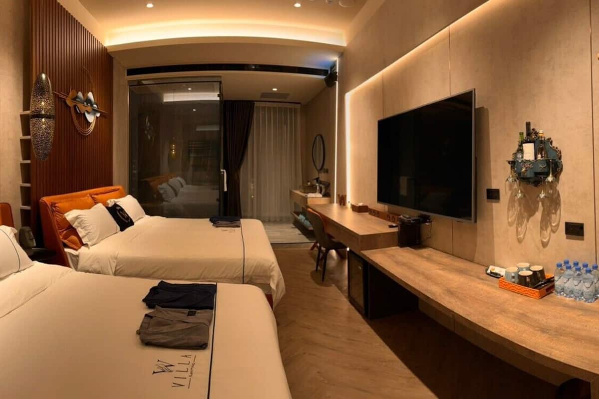 A hotel room with two beds, a TV, a wooden desk, and a minibar.
