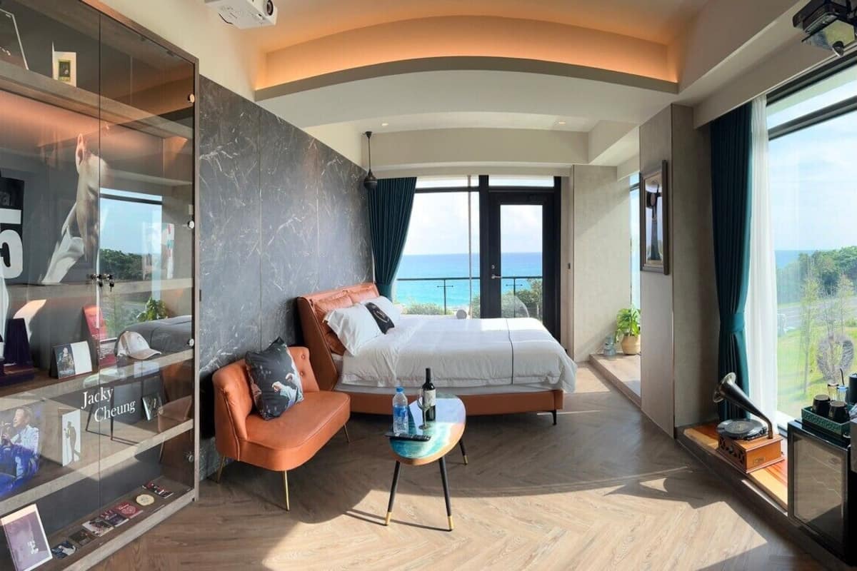 A modern hotel room with a large bed, a glass-enclosed vanity, and a view of the ocean.