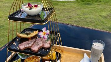 A three-tiered serving tray with food and drinks, a glass of milk, and cutlery on a wooden tray with a logo.