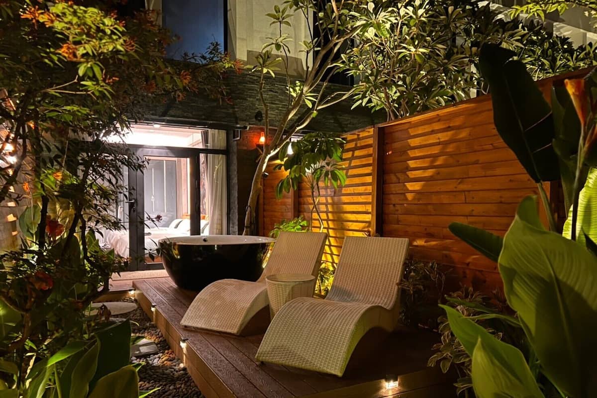 A serene outdoor seating area with a hot tub, wooden deck, and lush greenery.