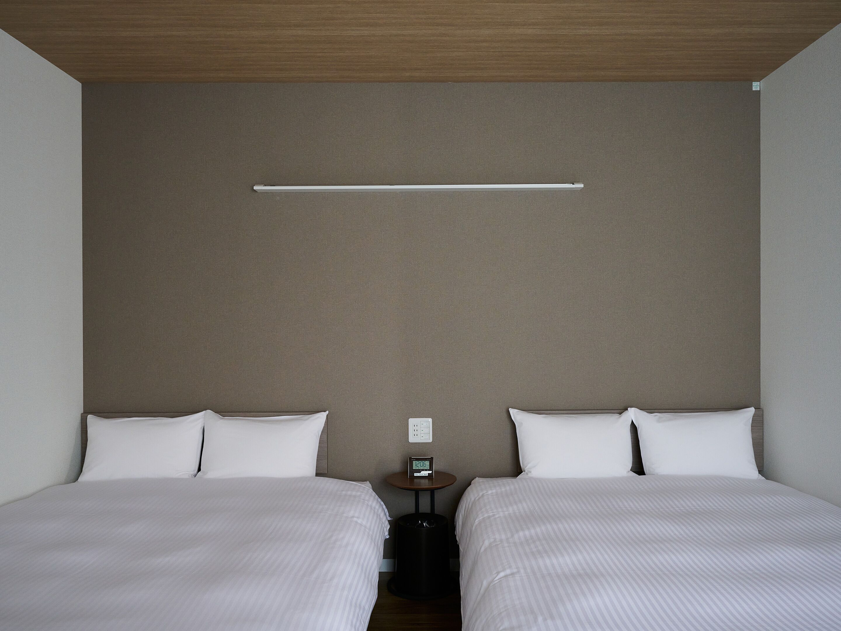 Een hotelkamer met twee bedden, een kleine tafel met een klok en een wandlamp.