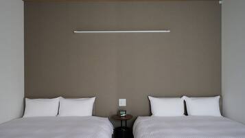 Een hotelkamer met twee bedden, een kleine tafel met een klok en een wandlamp.