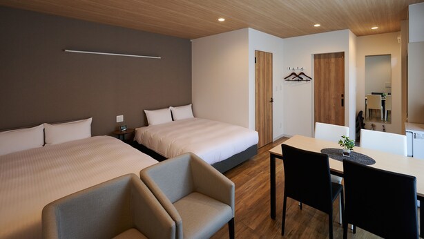 Habitación de hotel con dos camas, un escritorio y una silla. El techo es de madera y hay un espejo en la pared.