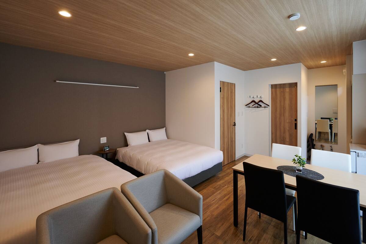 A hotel room with two beds, a desk, and a chair. There is a wooden ceiling and a mirror on the wall.