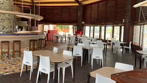 A spacious indoor dining area with high ceilings and large windows, featuring a mix of wooden and metal furniture.