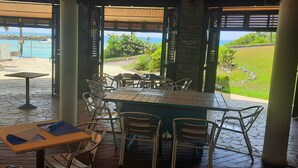An outdoor dining area with tables and chairs, a view of the ocean, and a pool in the background.