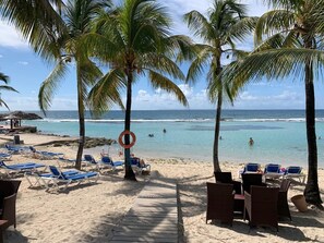 Een strand met palmbomen, een reddingsboei en blauwe ligbedden.