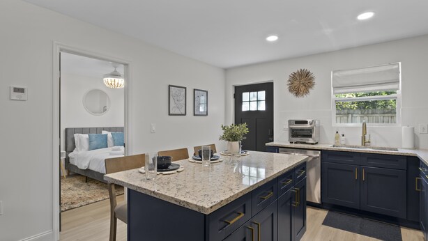 A modern kitchen with dark cabinets, a granite countertop, and a dining area with a bench and chairs. - Caffeinated Bungalito 75in TV- Walkable to Armature Works (Tampa)