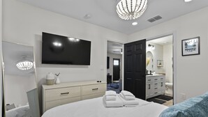 A modern hotel room with a large bed, a flat-screen TV, a dresser, and a bathroom visible through an open door. - Caffeinated Bungalito 75in TV- Walkable to Armature Works (Tampa)