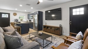 A modern living room with a dark blue sofa, a wooden coffee table, and a TV mounted on the wall. - Caffeinated Bungalito 75in TV- Walkable to Armature Works (Tampa)