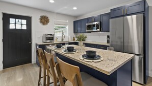 A modern kitchen with dark blue cabinets, stainless steel appliances, and a granite countertop. - Caffeinated Bungalito 75in TV- Walkable to Armature Works (Tampa)