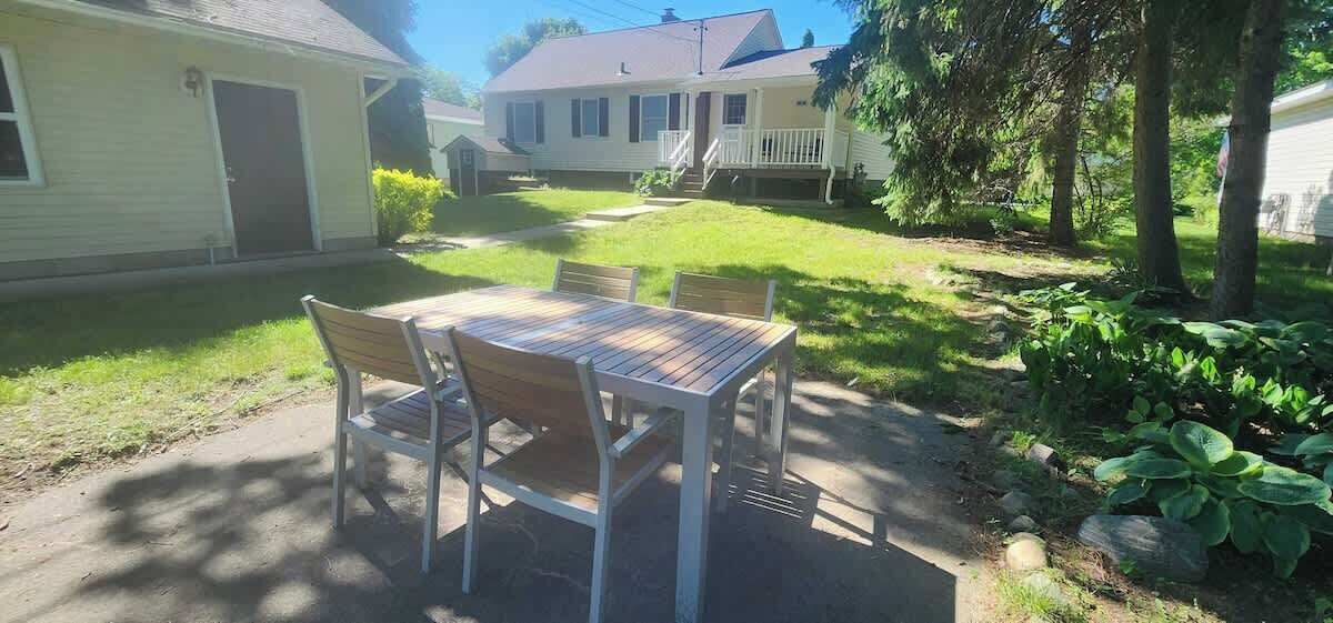 En terrasse med et bord og stole, omgivet af græsplæne og et hus i baggrunden.