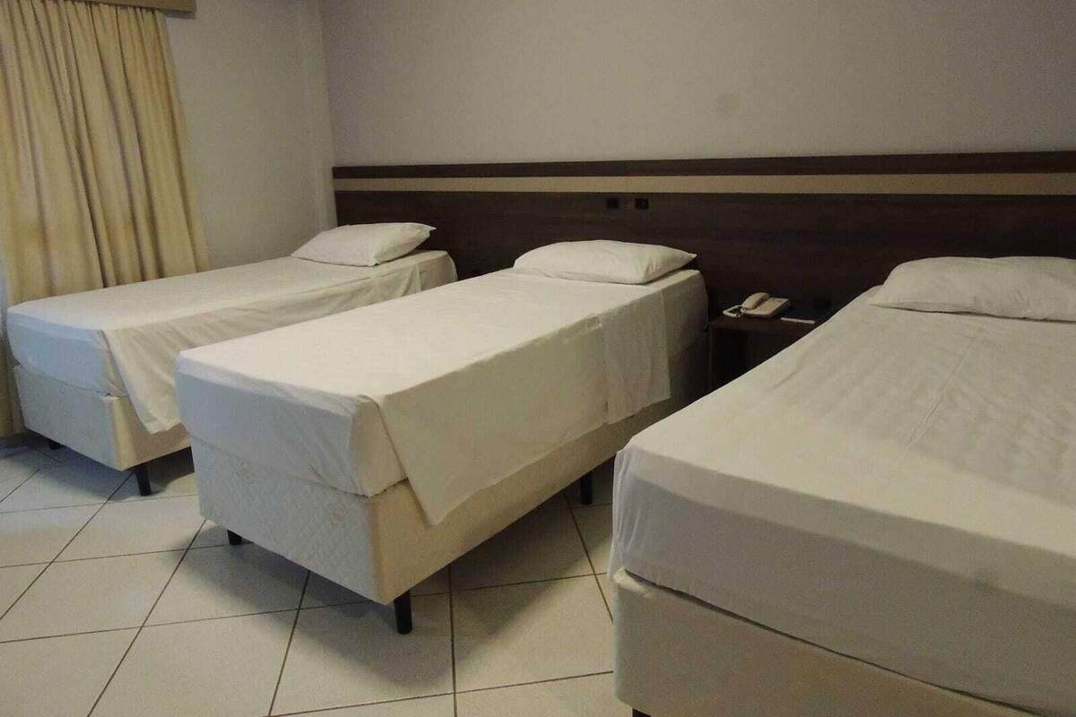 Habitación de hotel con tres camas individuales, una mesita de noche con teléfono y una cortina en la ventana.